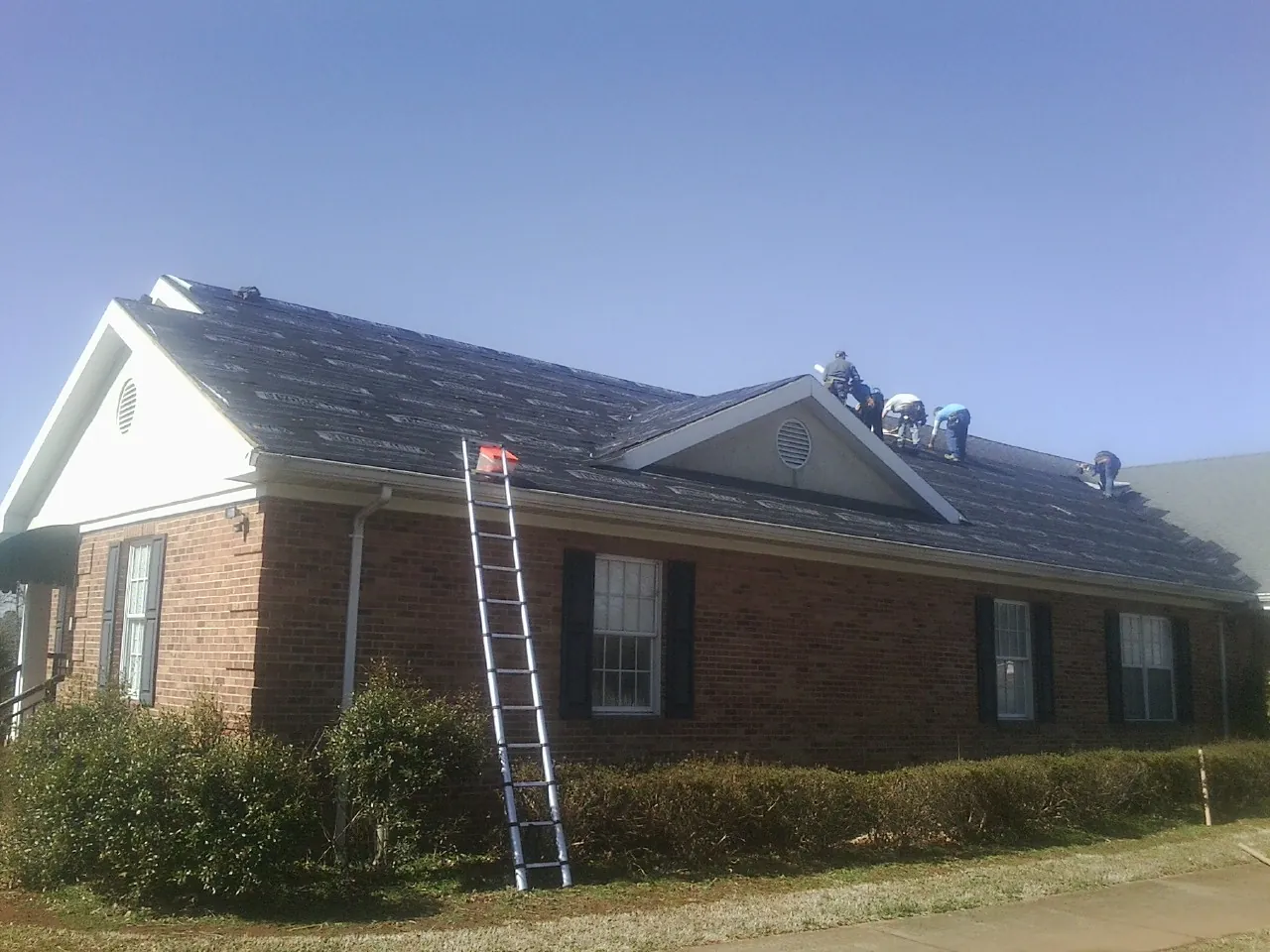 Crew tearing shingles off a brick ranch roof with a ladder set — Emergency Roof Repair work by our crew in Stoneboro