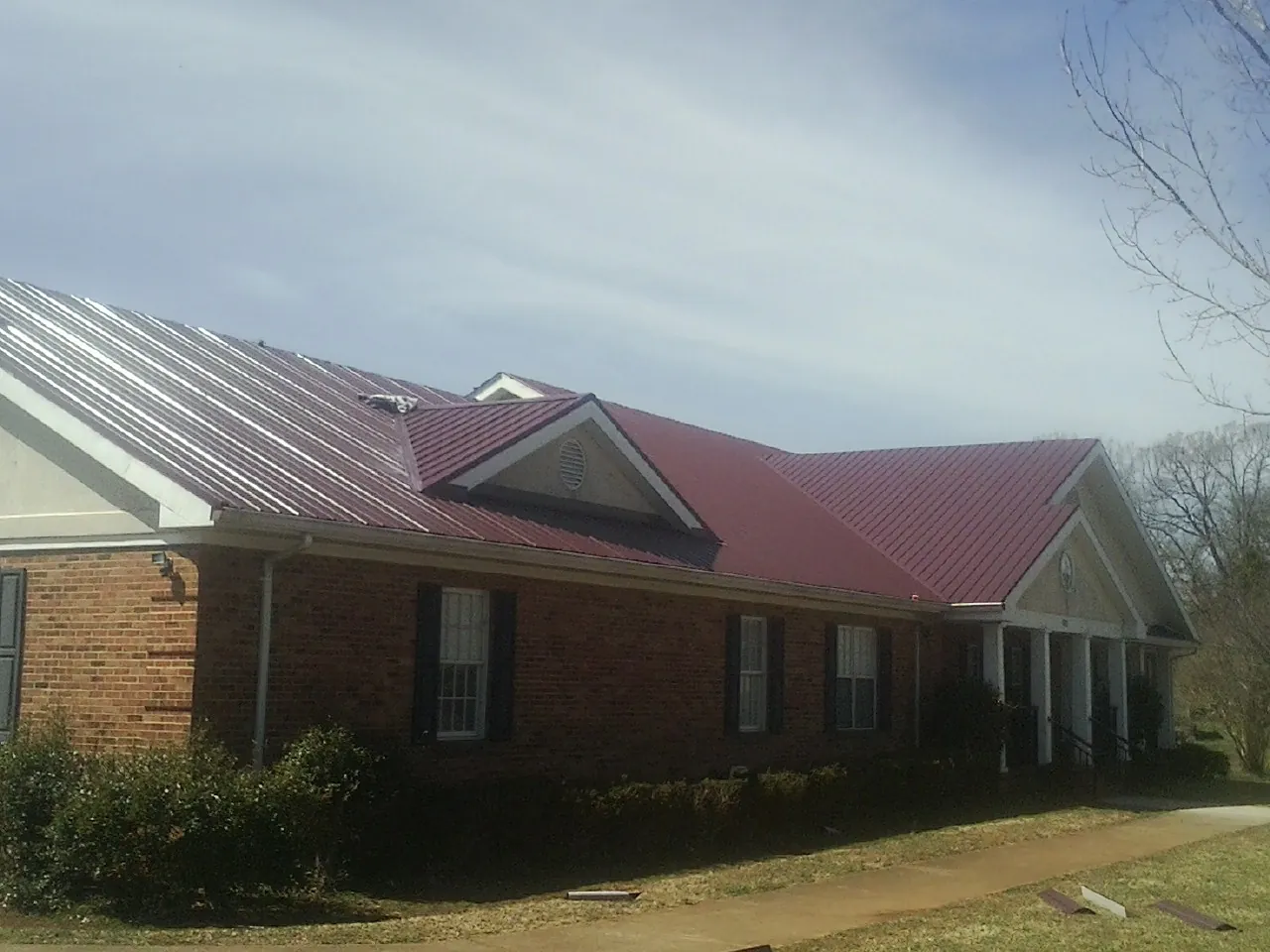 Red metal roof with gabled entries on a long brick building, from a Hail Damage Roof Repair job in Stoneboro