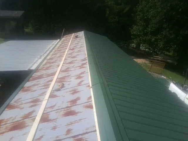 Old rusted panels beside newly installed green metal roofing — Wind Damage Roof Repair by Roofing Brothers in Stoneboro