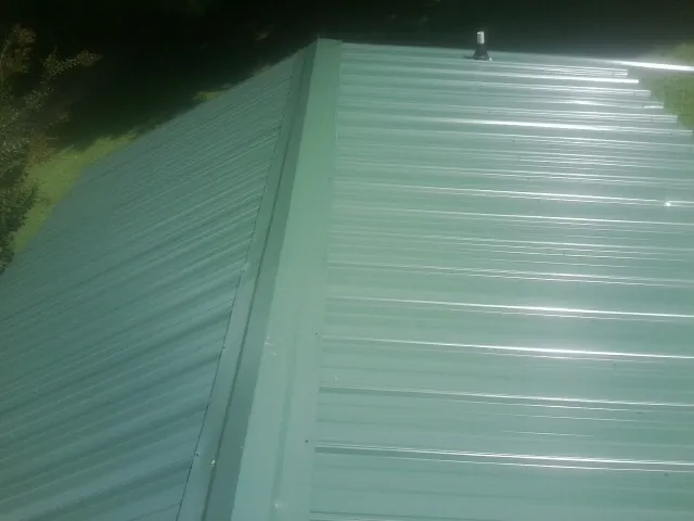 New green metal panels meeting at the ridge of a roof — Flat Roof Repair work by our crew in Stoneboro