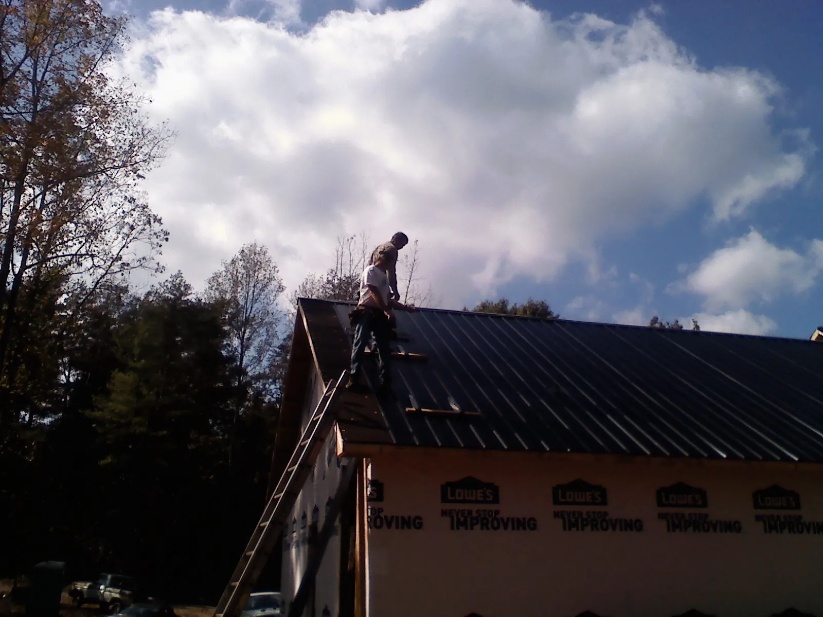 Roofer fastening dark metal panels high against a cloudy sky, from a Roof Inspection job in Stoneboro