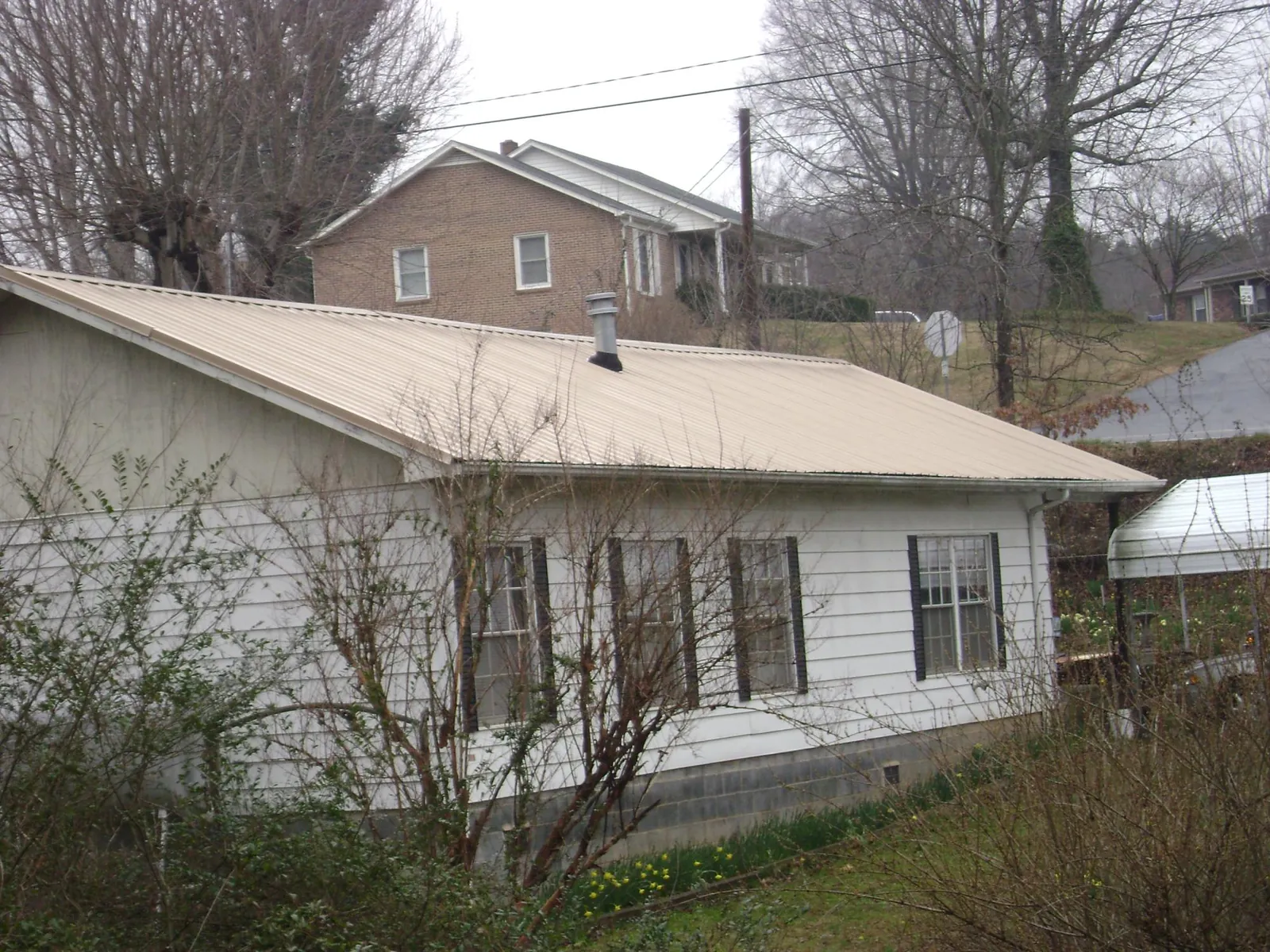 Tan metal roof on a white sided house set into a hillside — Commercial Roofing by Roofing Brothers in Stoneboro