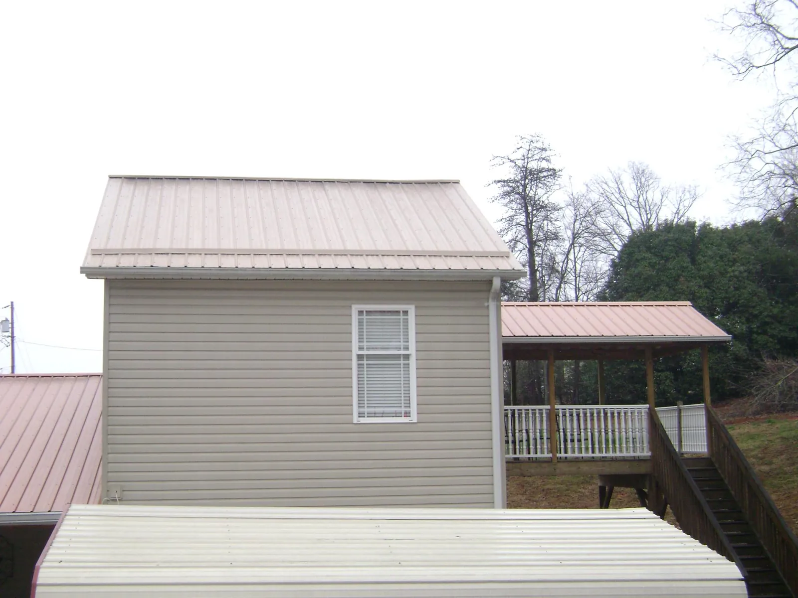 Tan metal roofs on a two story addition and attached porch, from a Roof Replacement job in Stoneboro